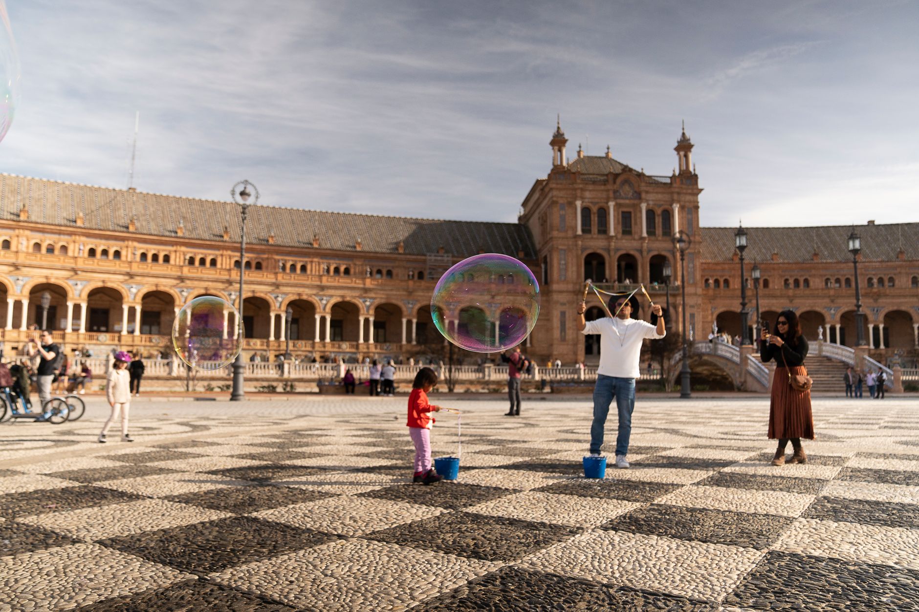 A joyful scene of people playing with bubbles at Plaza de España in Seville, Spain.