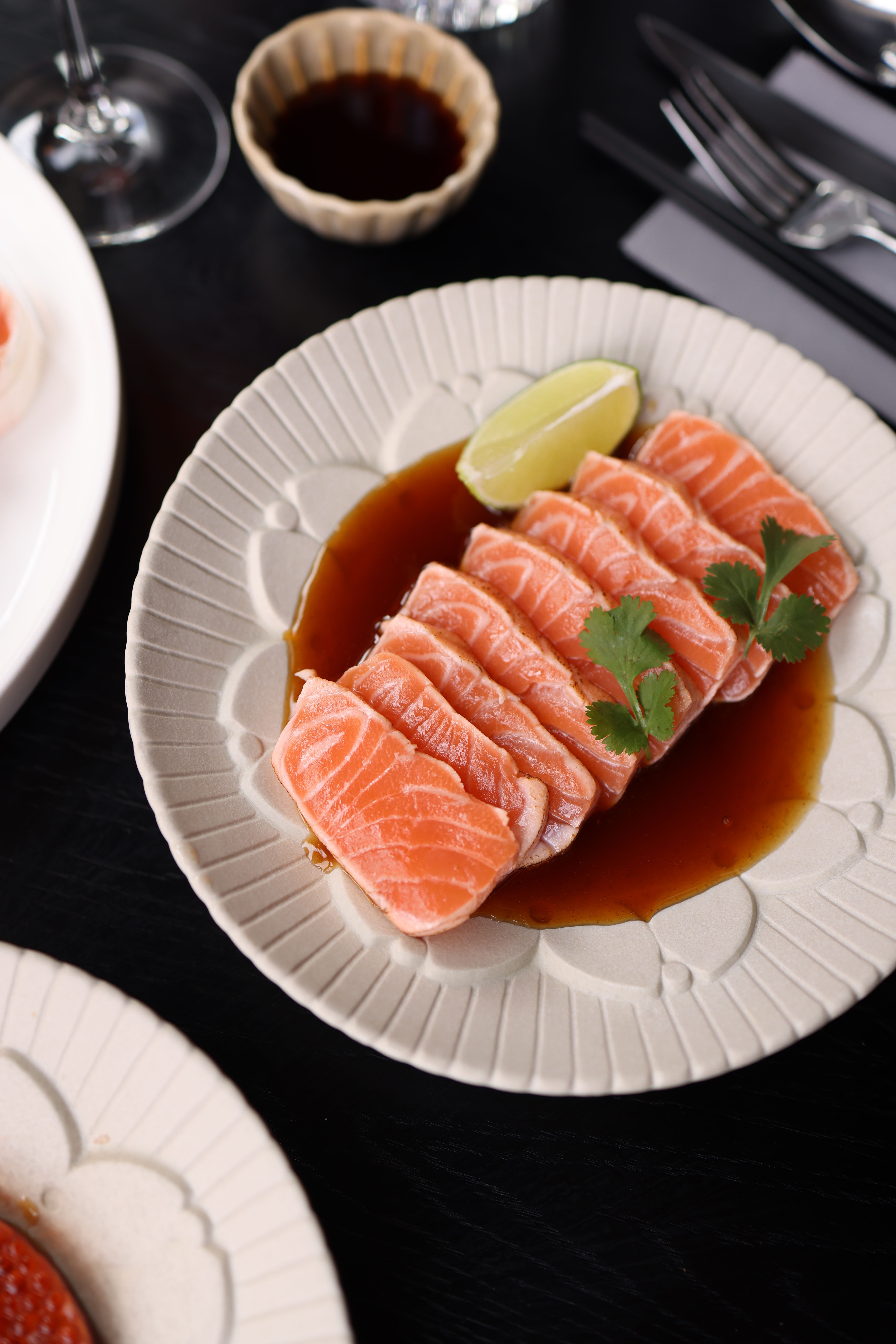 Fresh salmon sashimi served with soy sauce and lime garnish, perfect for seafood lovers.
