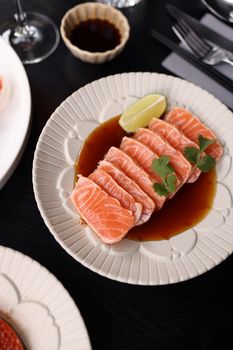 Fresh salmon sashimi served with soy sauce and lime garnish, perfect for seafood lovers.