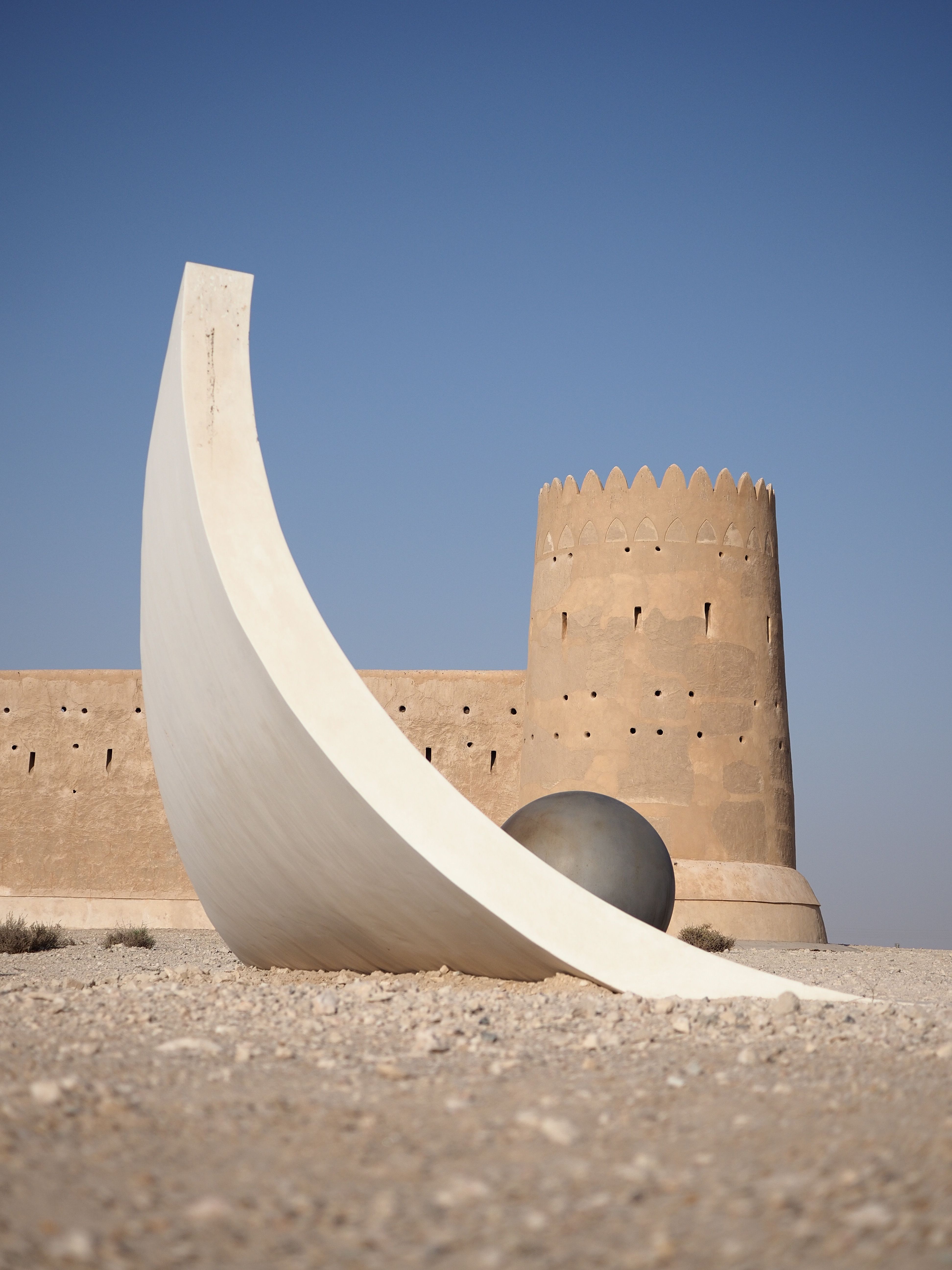 Modern sculpture and historic Al Zubarah Fort, Qatar under a clear blue sky.