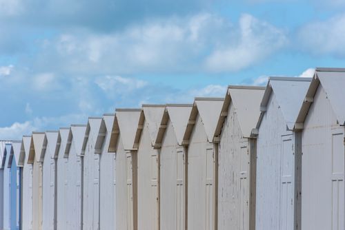Free White beach huts aligned under a blue sky with scattered clouds, capturing a serene coastal view. Stock Photo