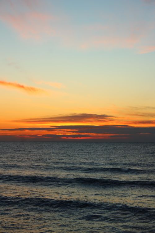 Free Serene ocean view at sunset with vivid orange and blue sky, capturing peaceful waves. Stock Photo