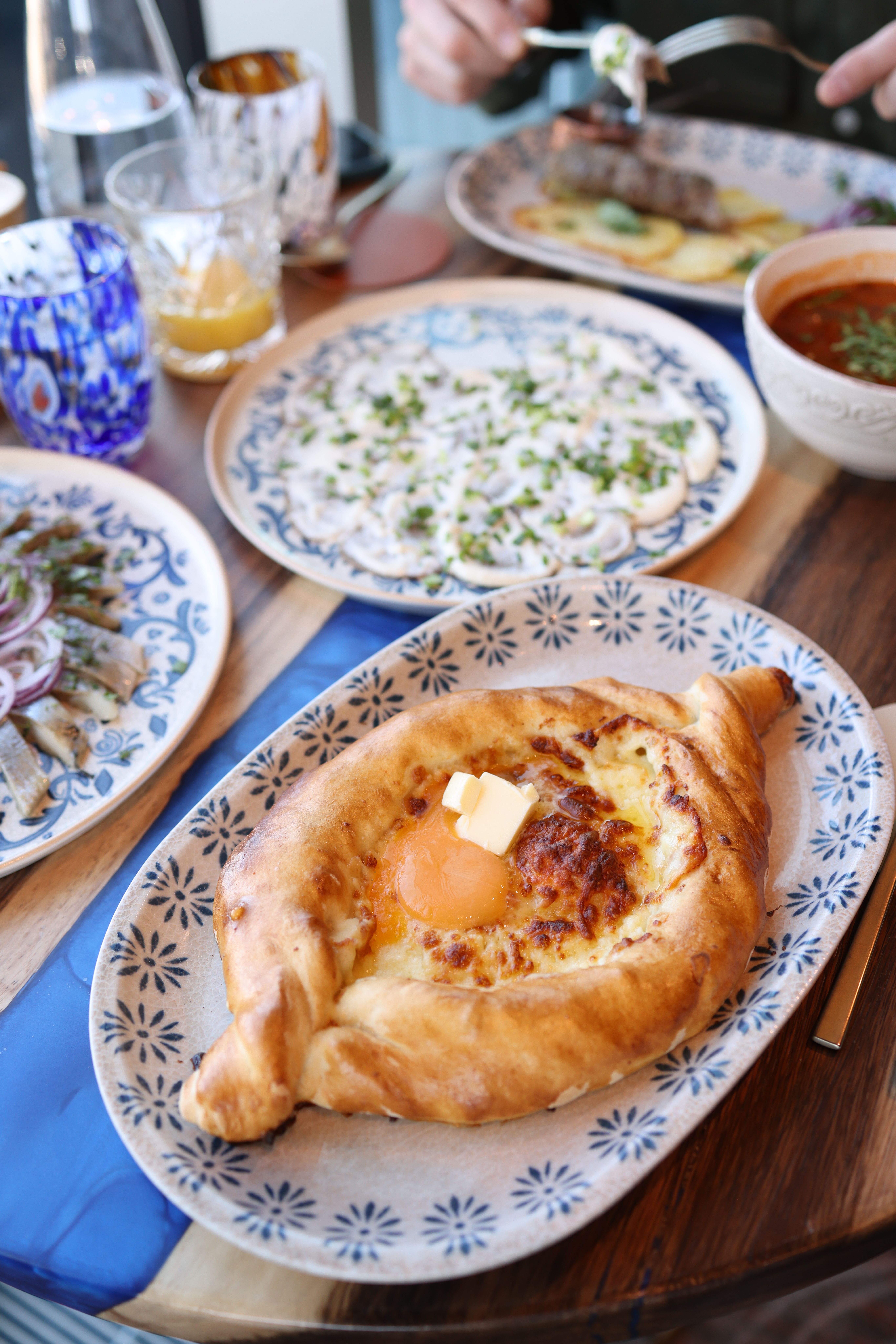 Delicious Georgian khachapuri with egg served among various dishes on a wooden table.