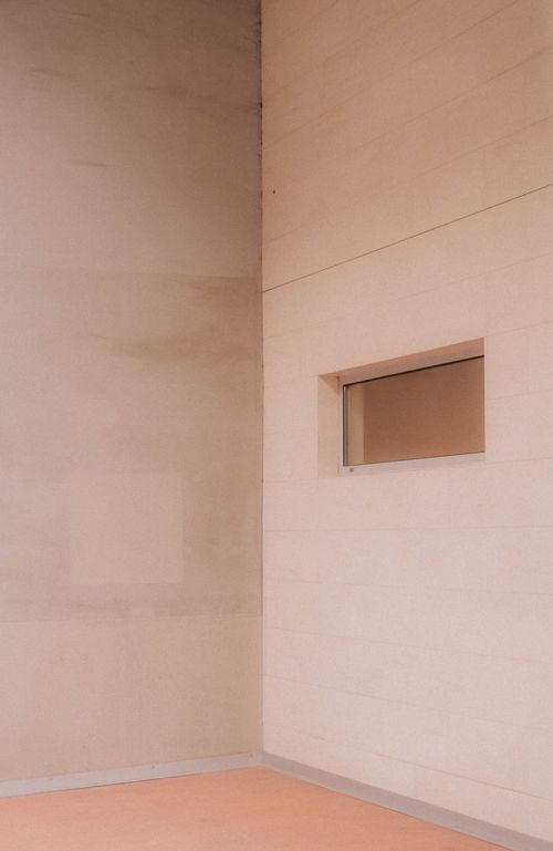 Free A modern, minimalist architectural wall featuring a small window in soft tones. Stock Photo