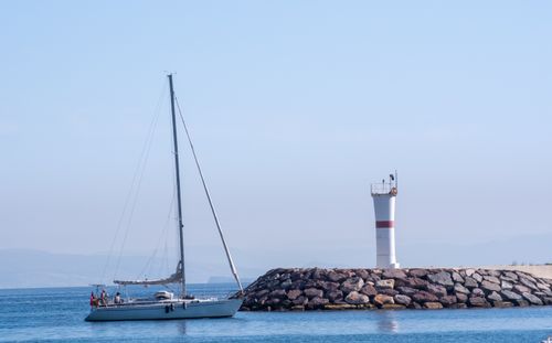 Free Scenic view of a sailboat near a lighthouse in Foça, İzmir, Türkiye during the day. Stock Photo