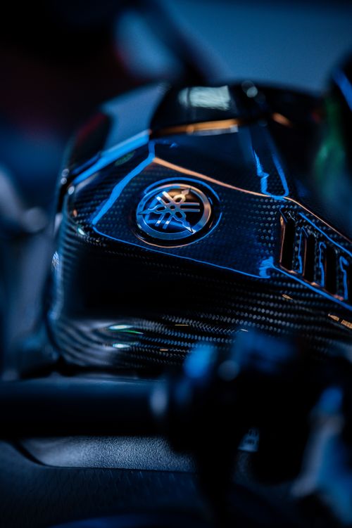 Free Detailed shot of a motorcycle part with a carbon fiber texture and metallic logo under blue lighting. Stock Photo