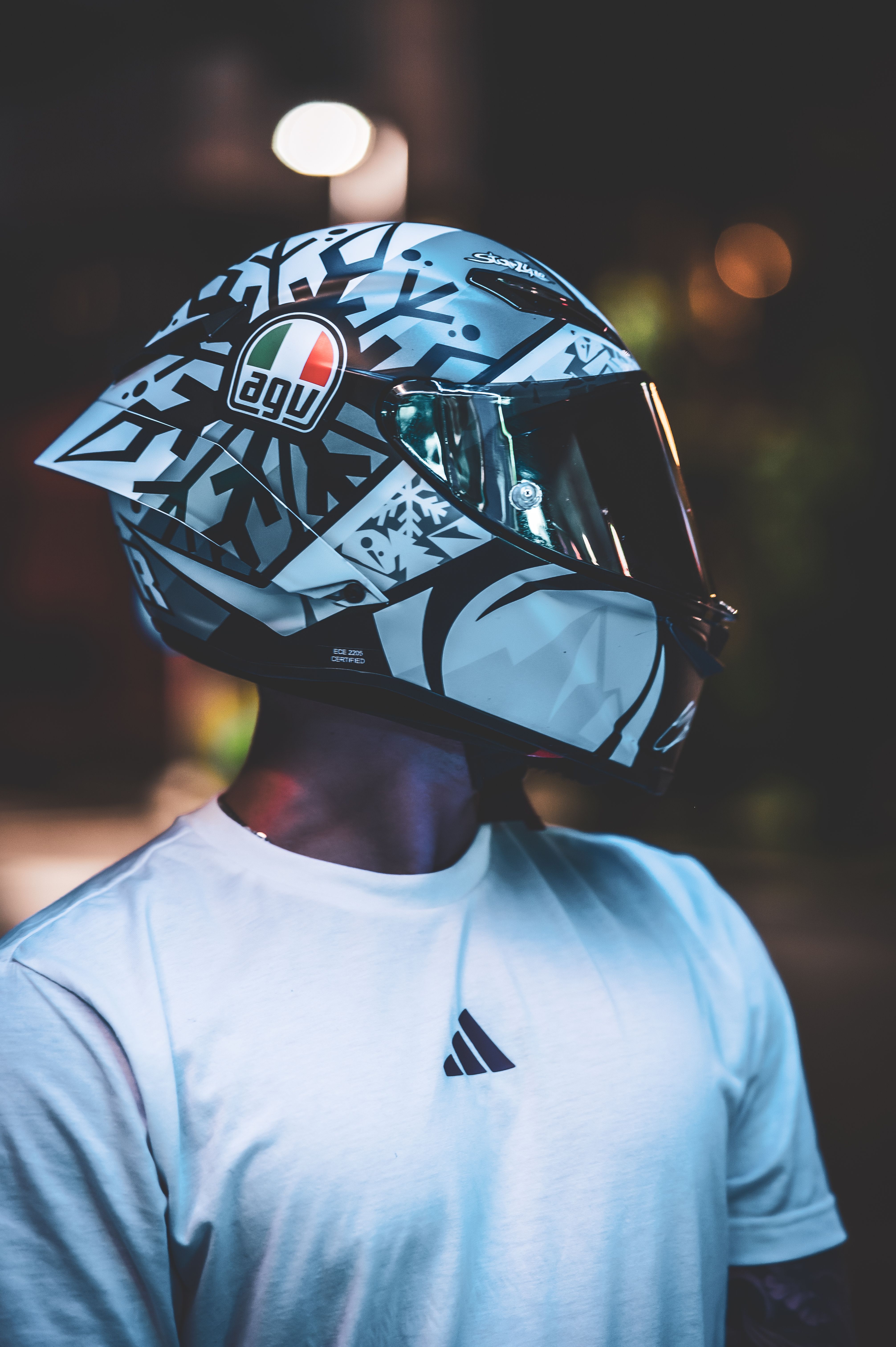 A sleek modern motorcycle helmet worn by a person in a white shirt under urban night lights.