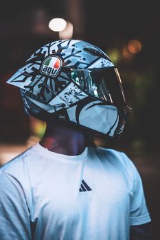A sleek modern motorcycle helmet worn by a person in a white shirt under urban night lights.