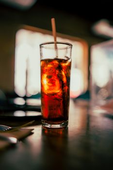 A tall, refreshing glass of iced cola with a straw on a warm day.