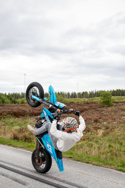 Free Daring motorcycle wheelie performed on a scenic rural road. Stock Photo