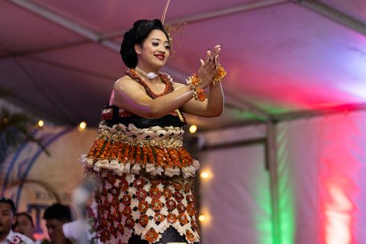 A woman performs a traditional Polynesian dance, adorned in vibrant cultural attire under festive lighting.