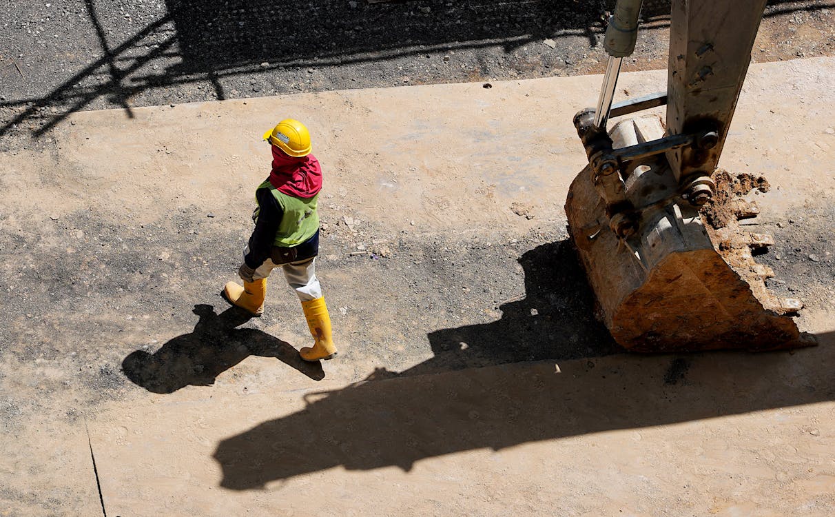 High Angle Photo of Person Walking Near Backhoe