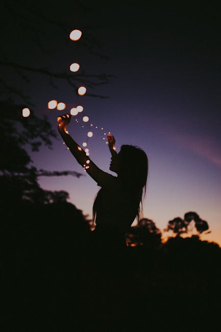 Silhouette of a woman holding fairy lights against a twilight sky in São Paulo, creating a magical mood.
