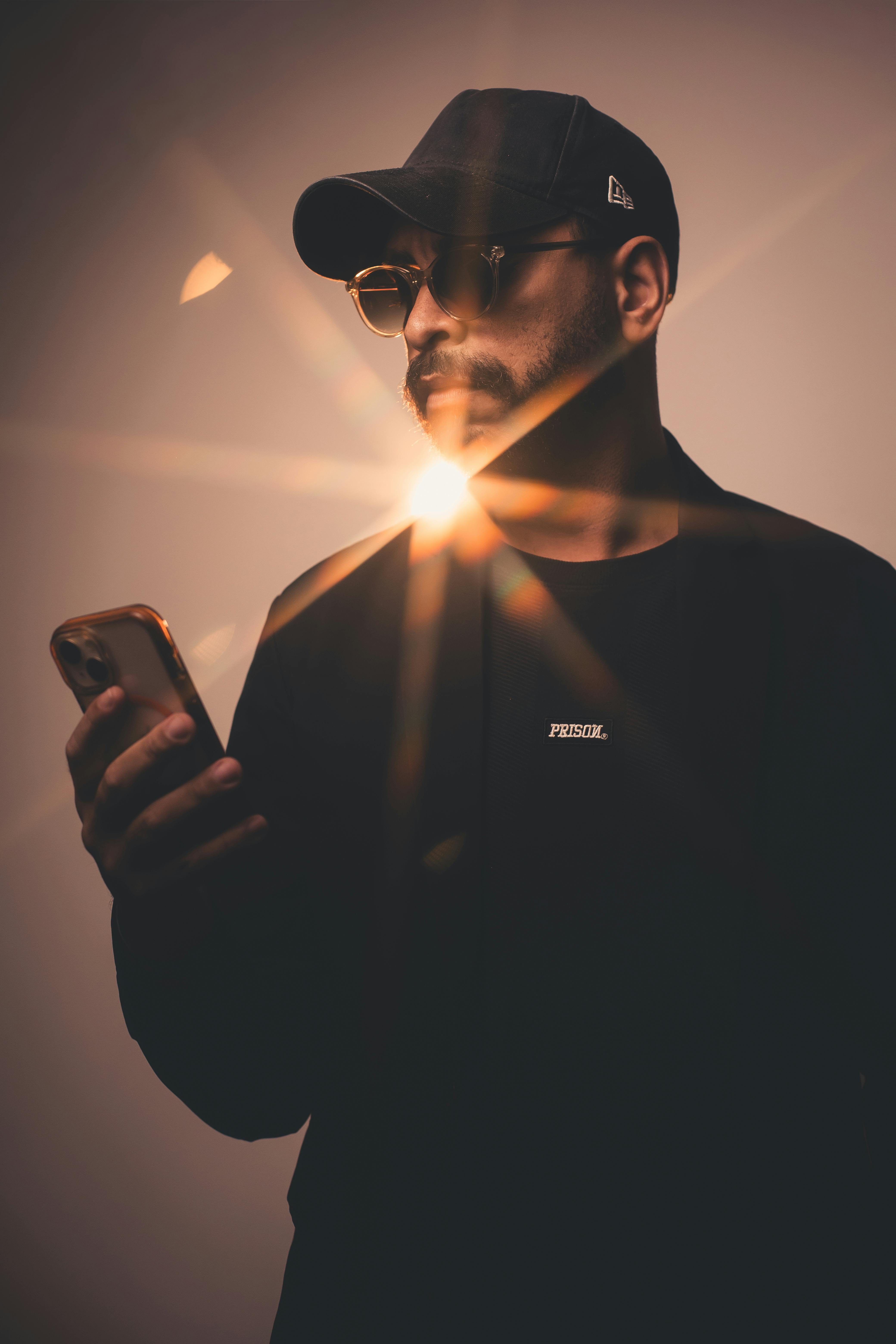 A modern portrait of a stylish man in sunglasses using a smartphone, accented by a sun flare.