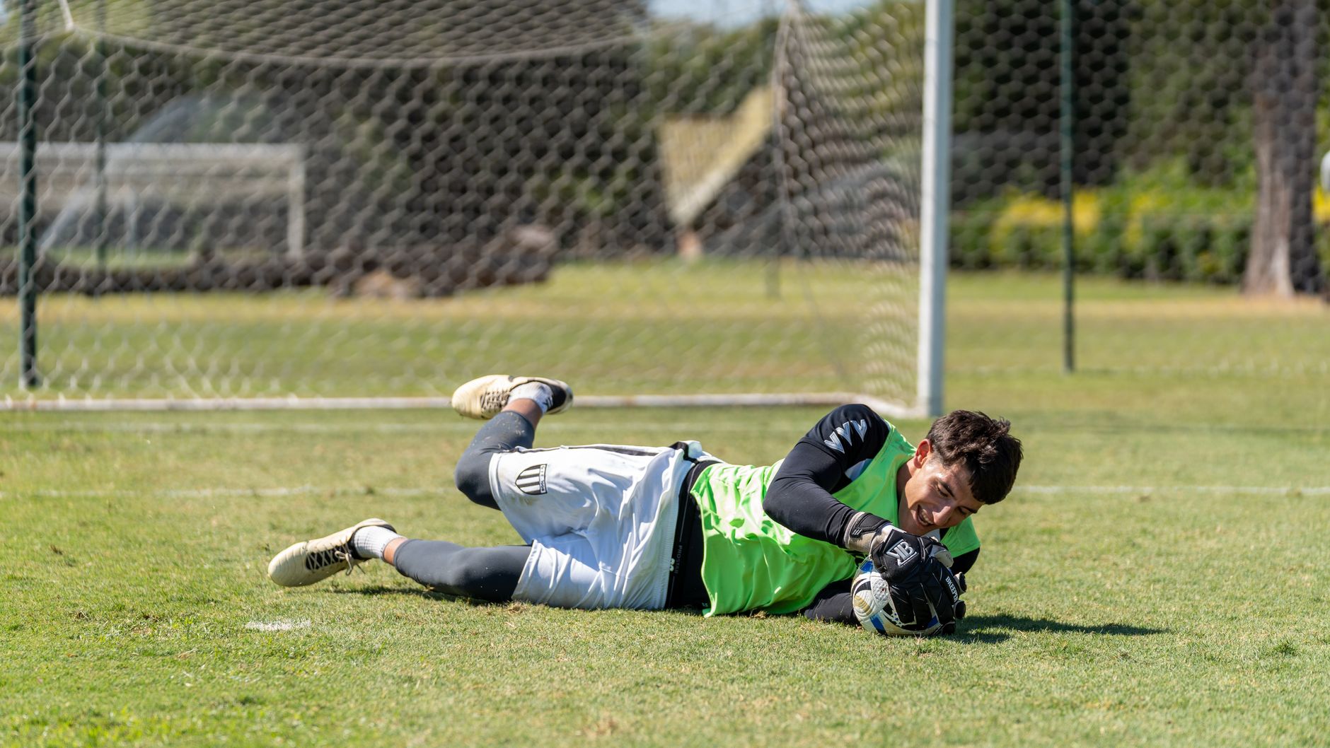 Soccer goalkeeper in action, making a save on the outdoor field during a sunny day.