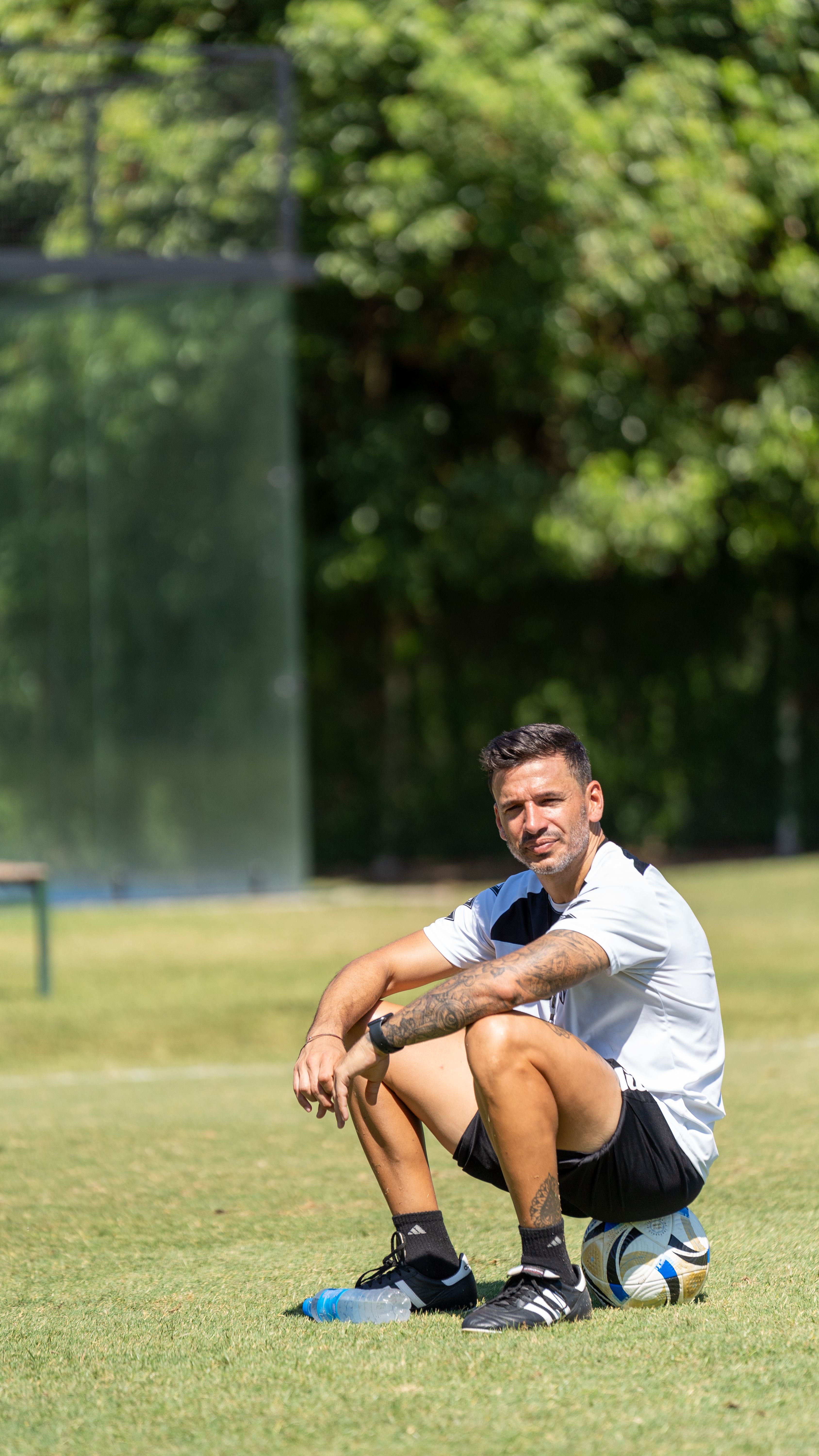 Soccer player sitting with a ball on a sunny field, enjoying a break.