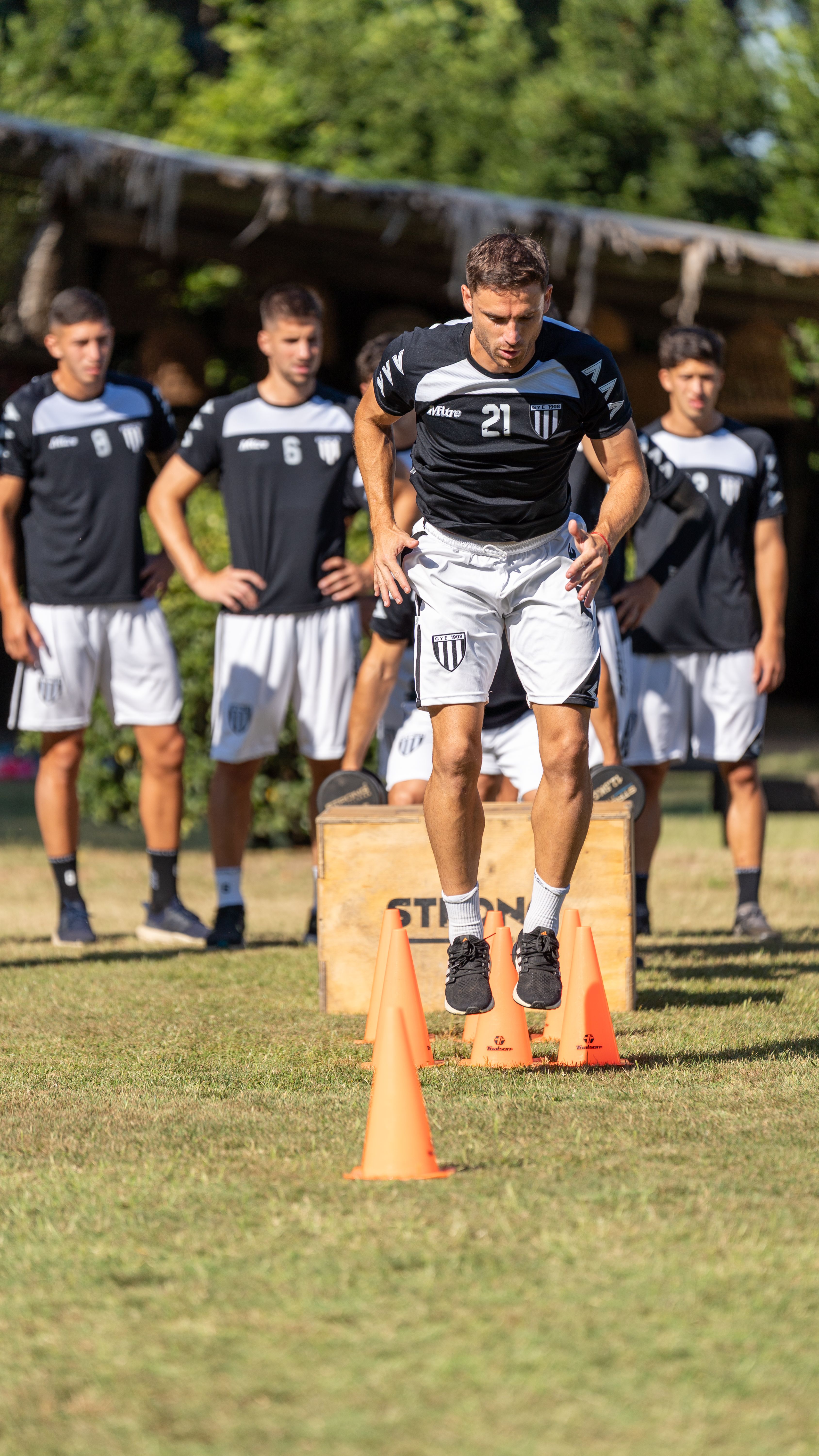 Group of young men performing outdoor fitness training in summer, focusing on agility and teamwork.