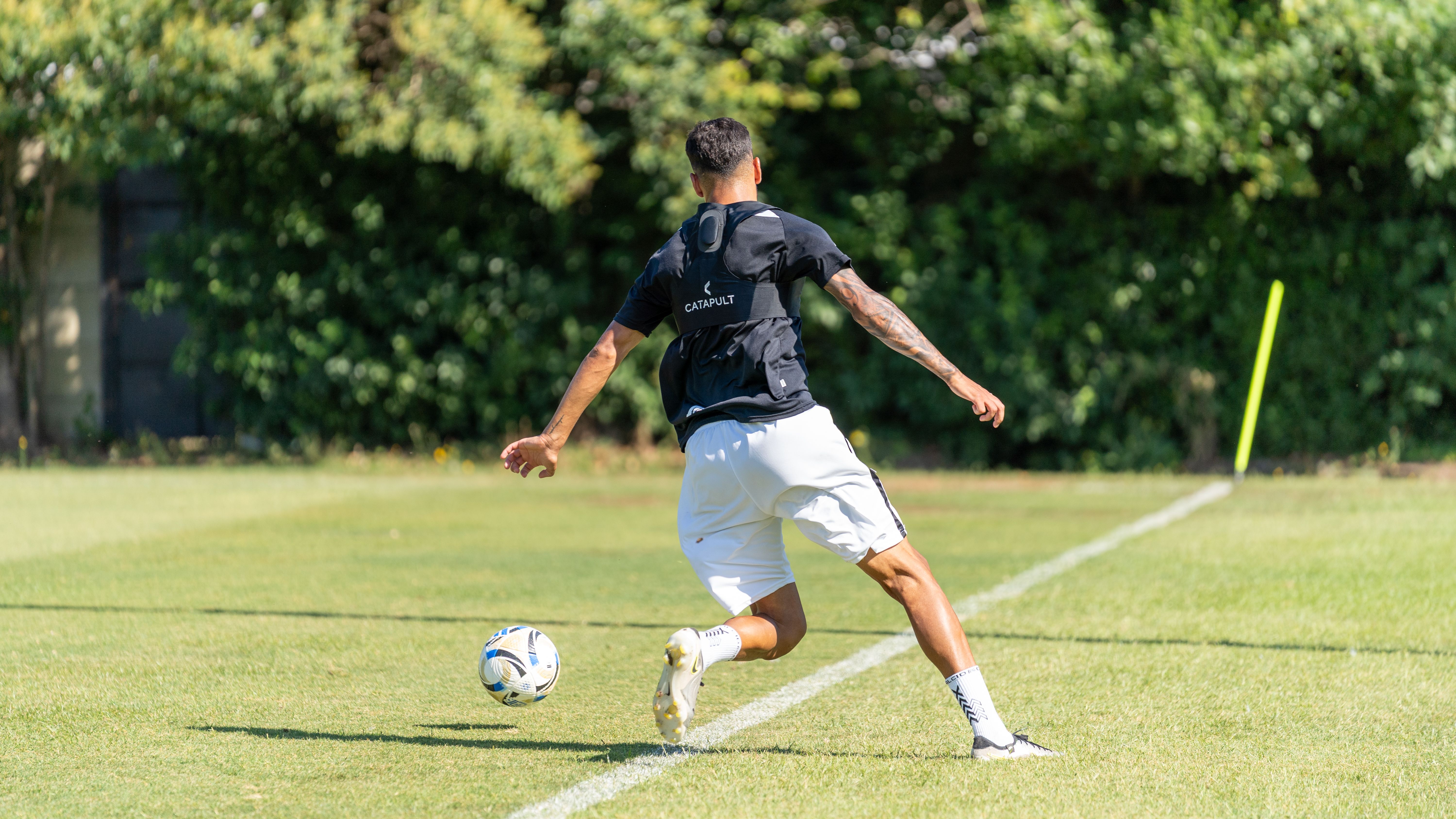 Soccer player training outdoors on a sunny day, kicking a ball.
