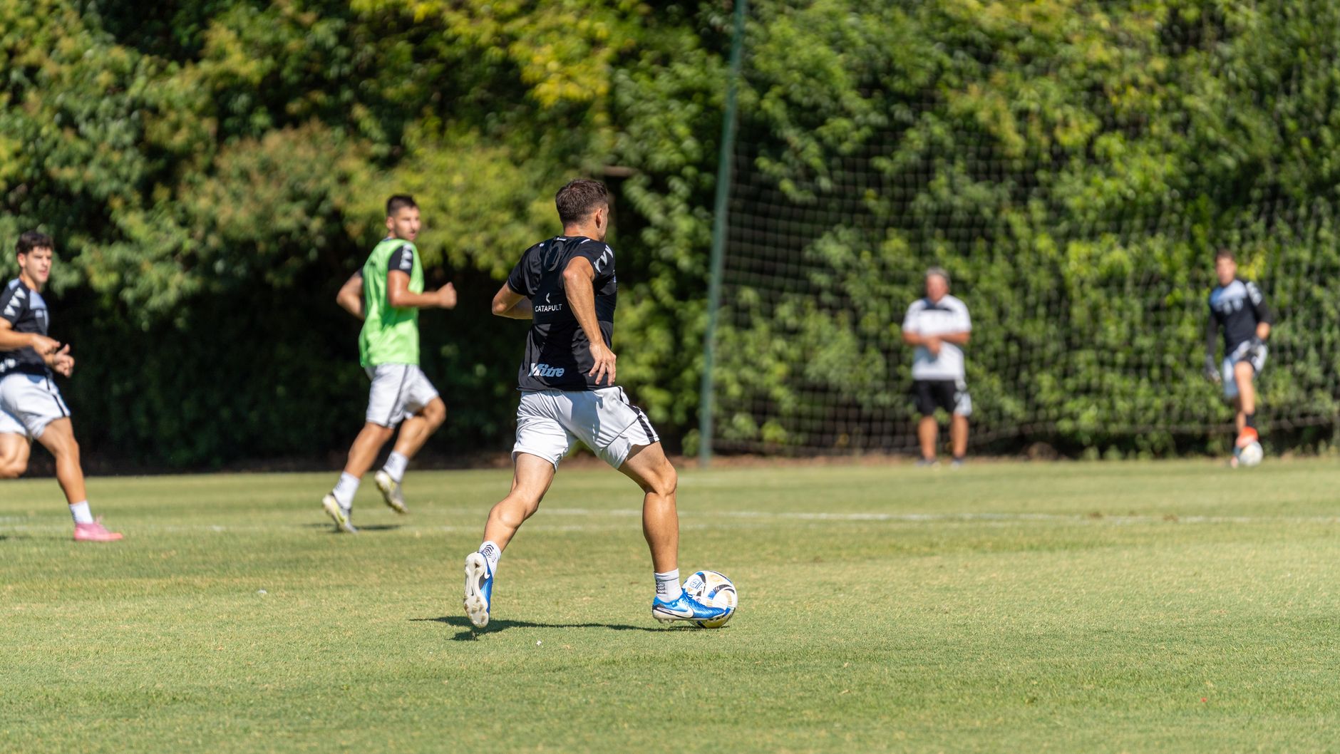 Group of male soccer players practicing on a sunny outdoor field with lush green background.