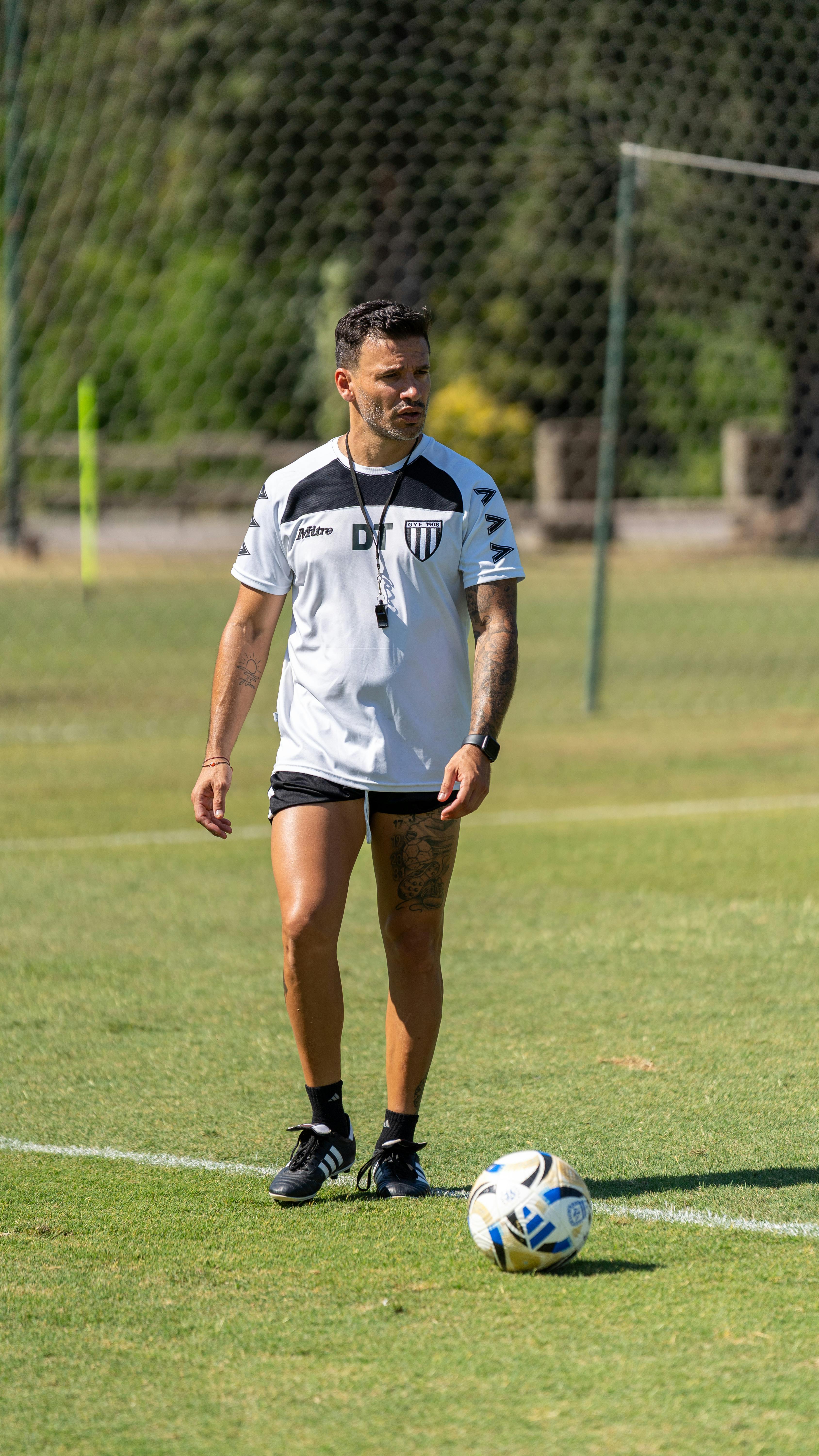 A soccer coach standing on a grass field preparing for training.