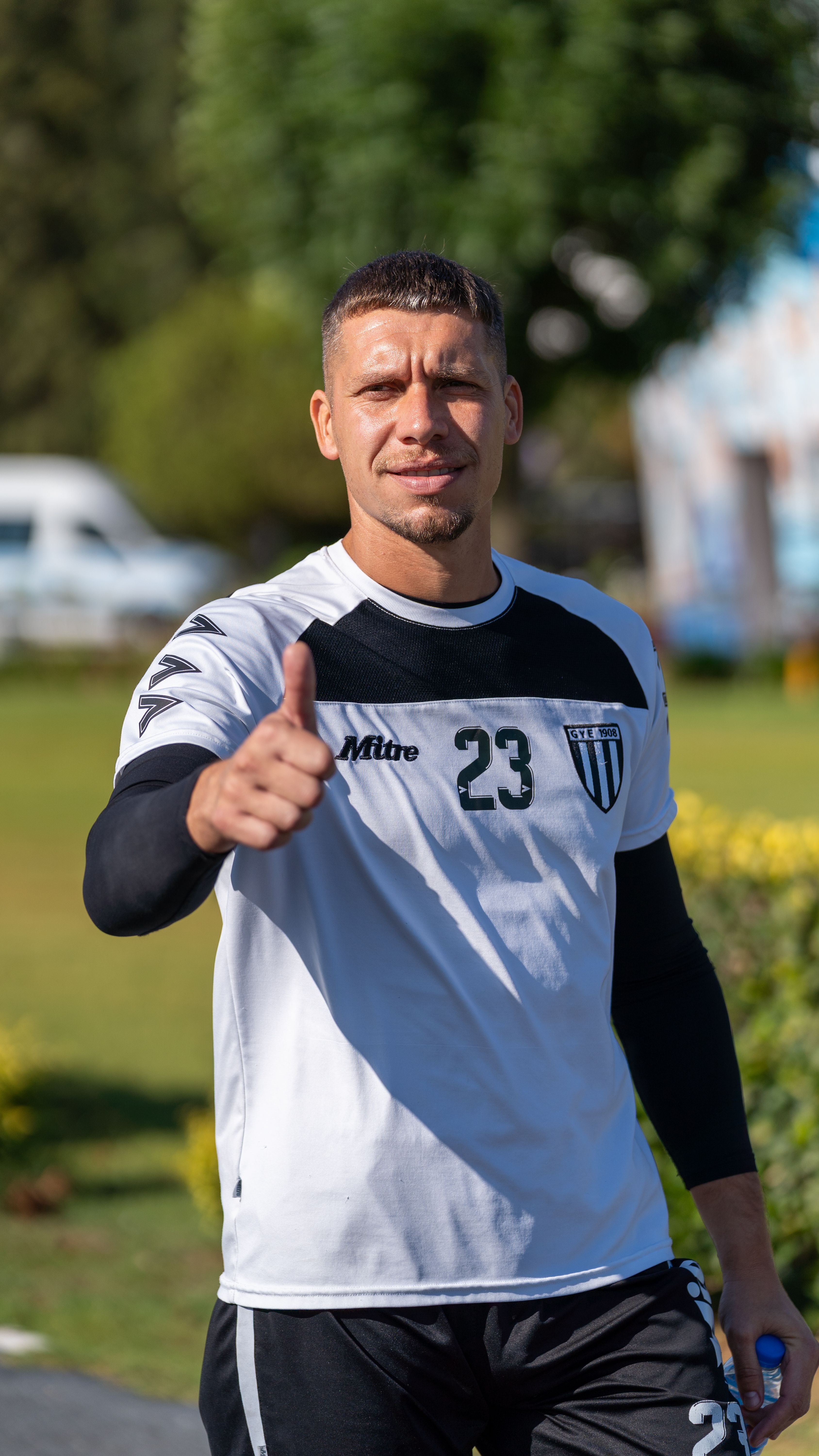 A soccer player in training gear gives a thumbs up in a sunny outdoor setting.