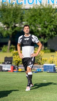 Male soccer player in training gear outdoors, hands on hips, sunny day.