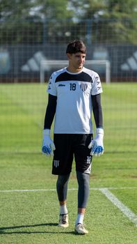 Goalkeeper in training on sunny soccer field wearing team jersey.