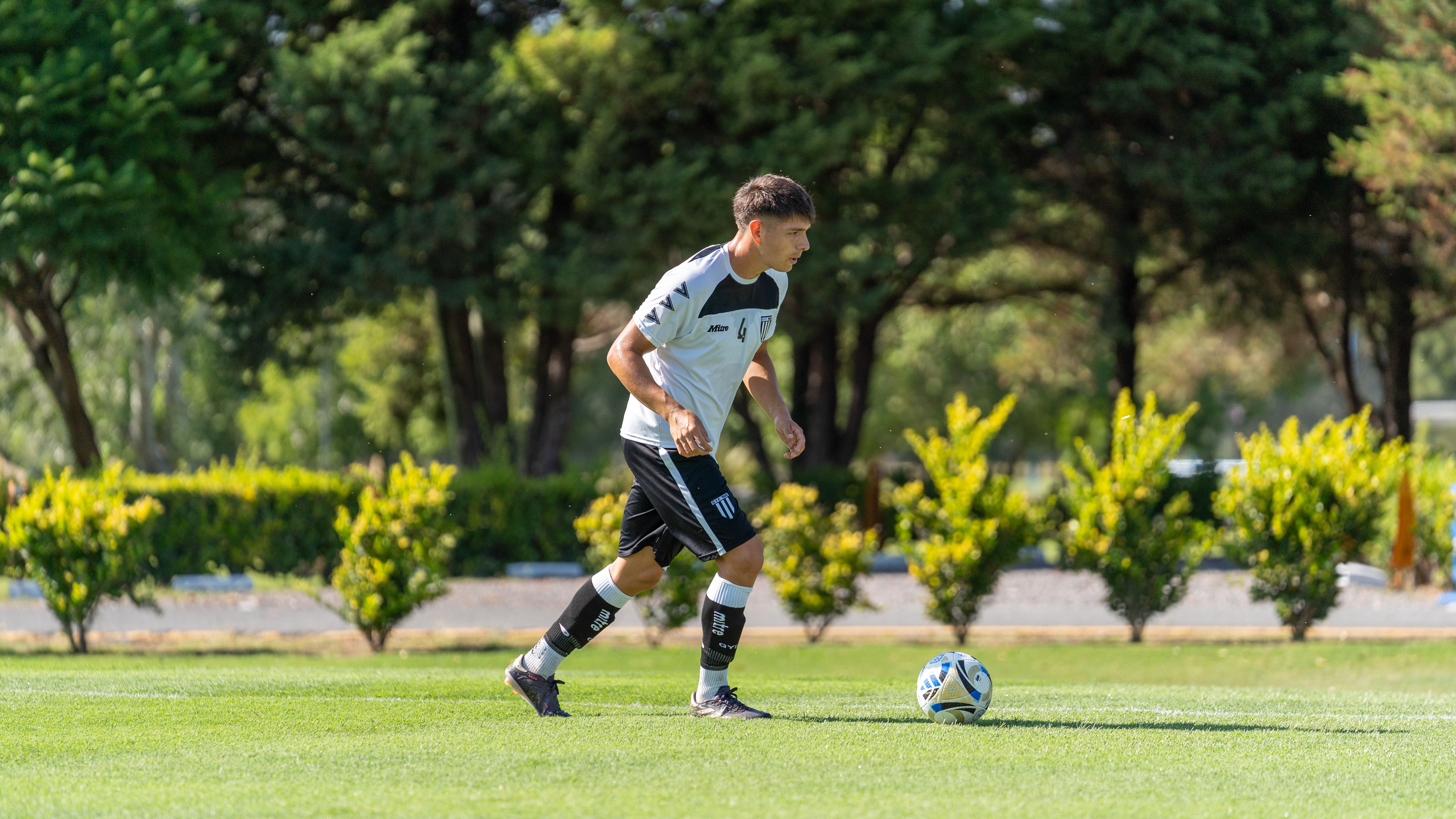 A young male soccer player dribbling a ball on a lush green outdoor field.