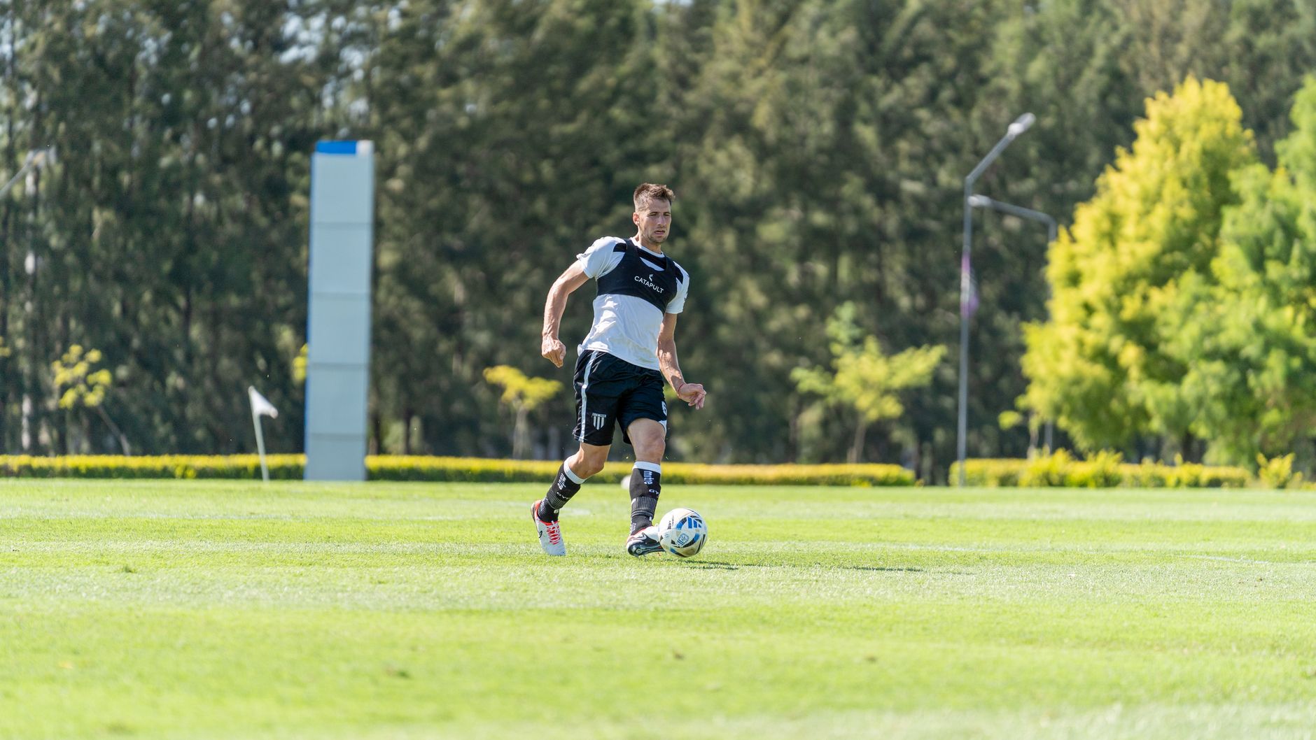 A football midfielder completing acceleration drills on a wet training pitch before sunrise