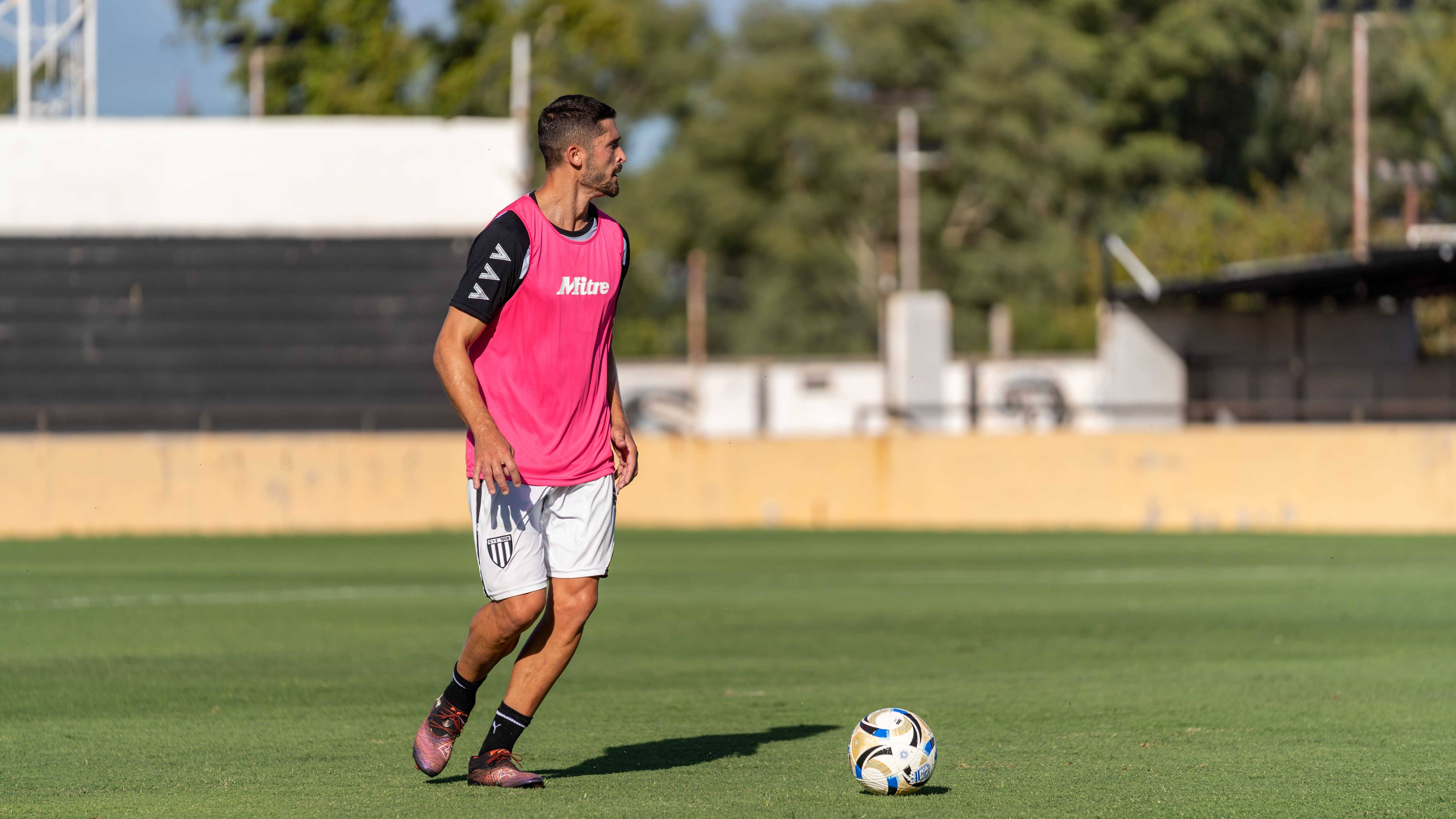 Professional soccer player practicing dribbling skills on an outdoor field during the day.