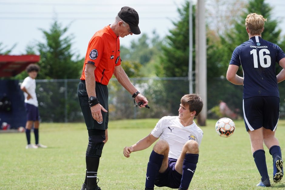 A soccer referee assists an injured player on a sunny outdoor field.