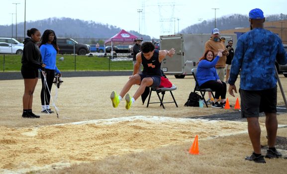 A young athlete executing a long jump outdoors with spectators watching.