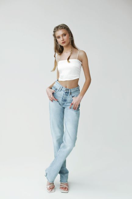 Elegant young woman in white top and jeans posing confidently in a minimalist studio setting.