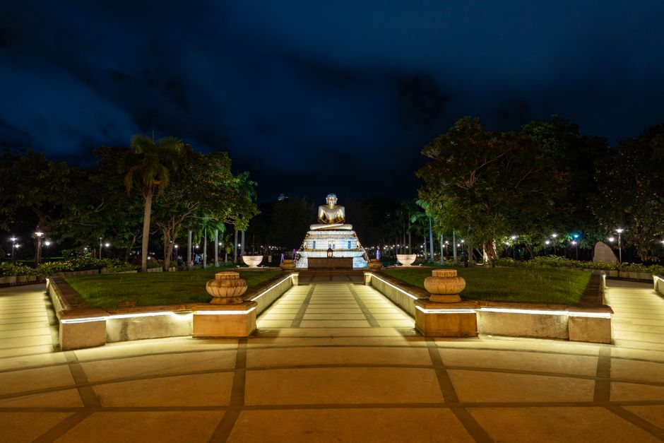 A serene nighttime view of an illuminated Buddha statue surrounded by lush greenery in Colombo, Sri Lanka.