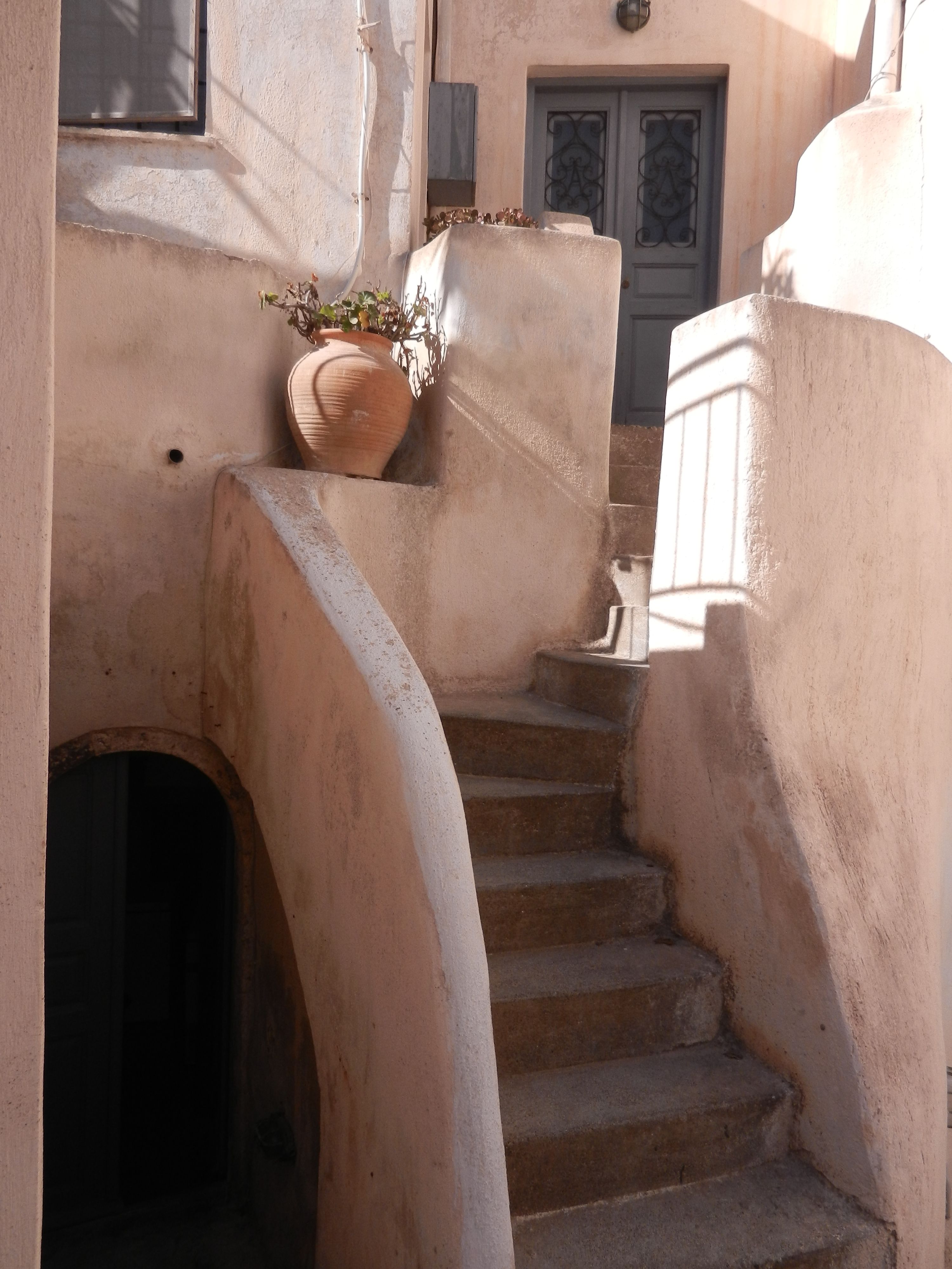 Charming rustic staircase with a clay pot under sunlight, exuding Mediterranean charm.
