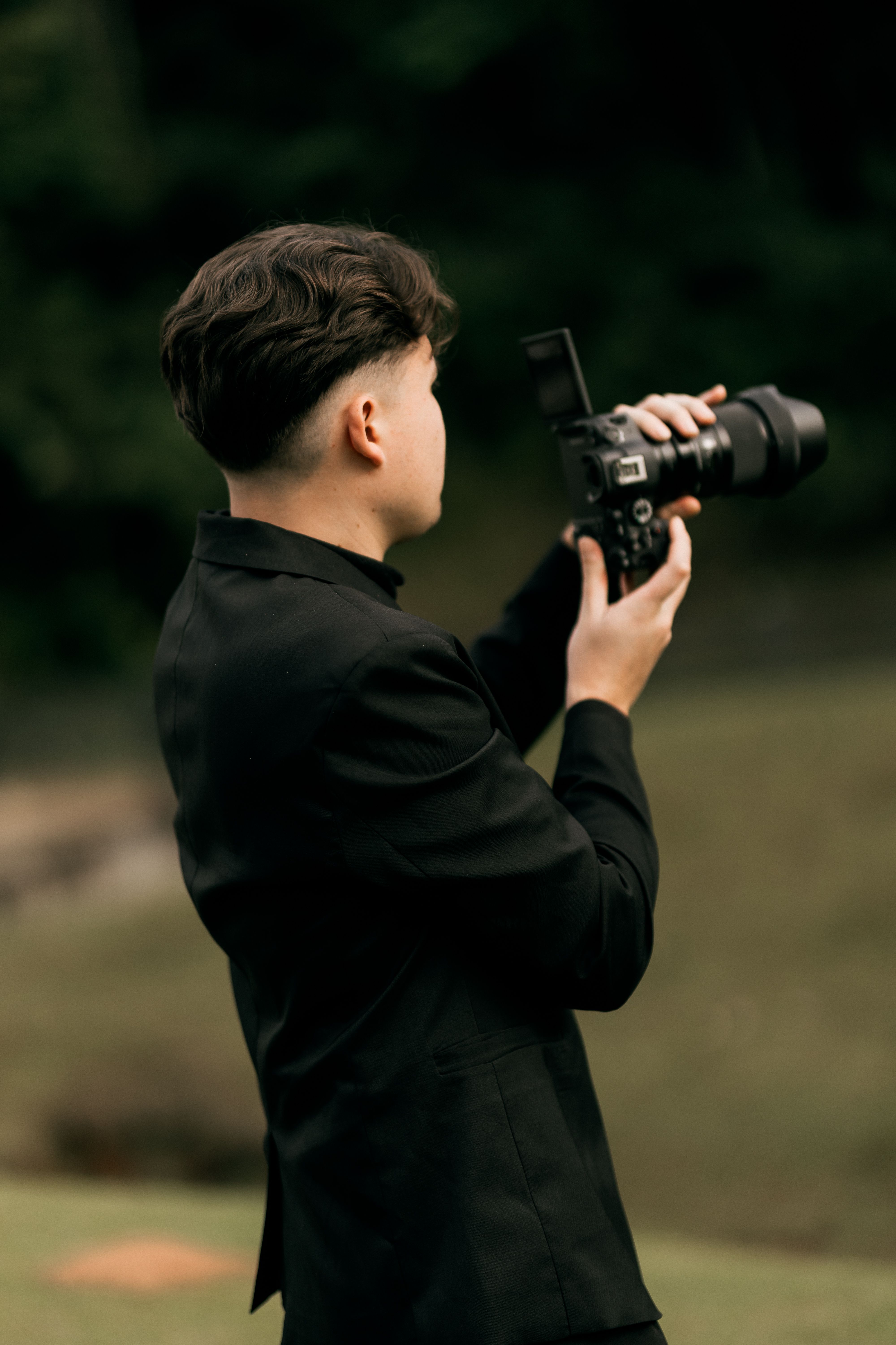 Photographer in a sleek black suit focuses on capturing a serene nature scene with a professional camera.