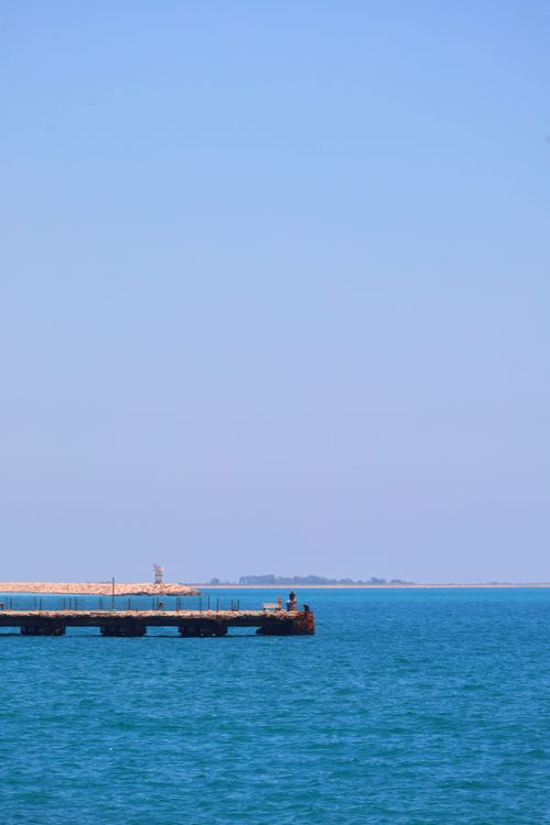 Free A calming scene of a pier extending into the tranquil blue sea under a clear sky. Stock Photo