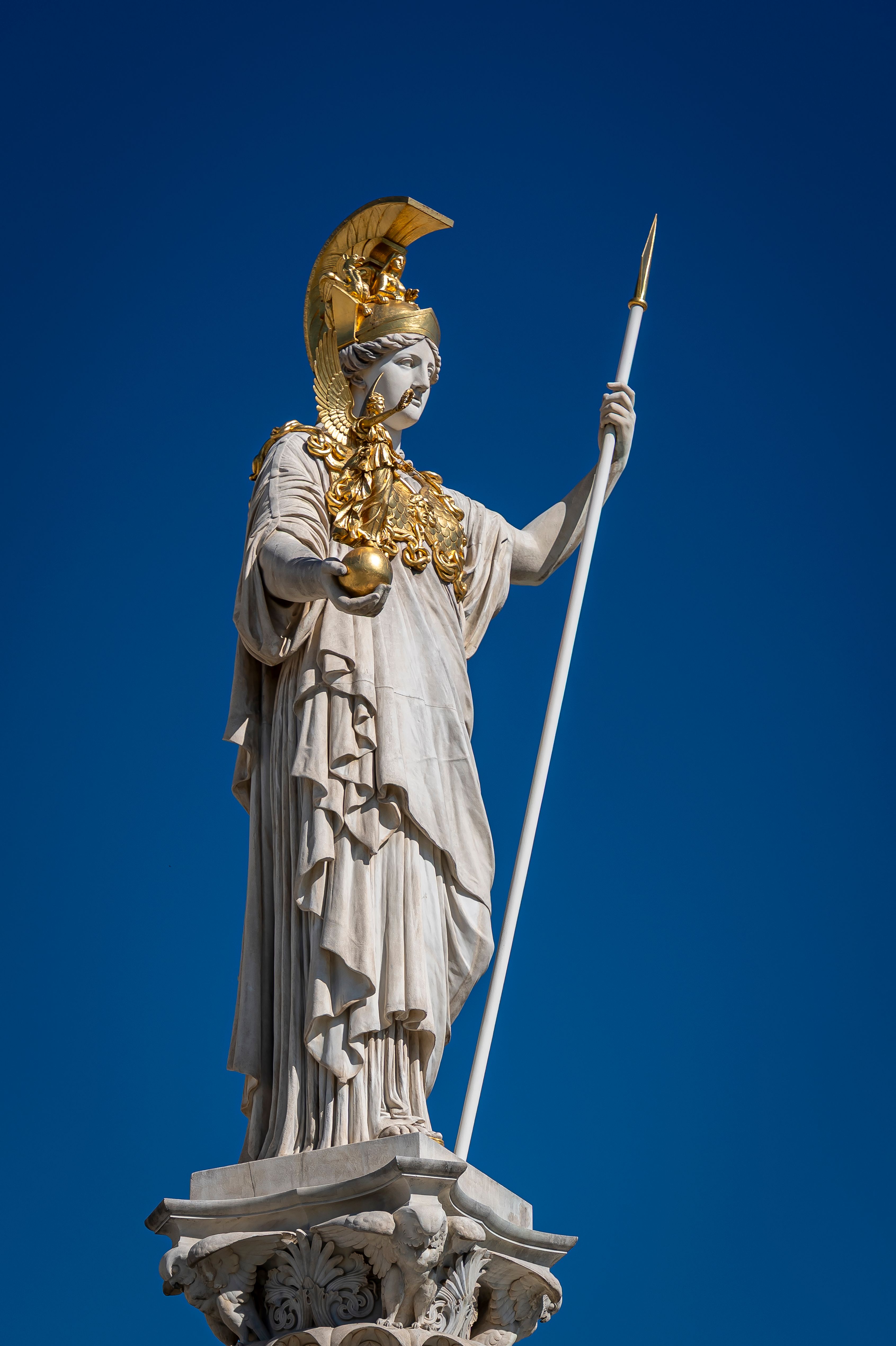 Elegant marble statue of Athena with golden details under a clear blue sky, symbolizing wisdom.