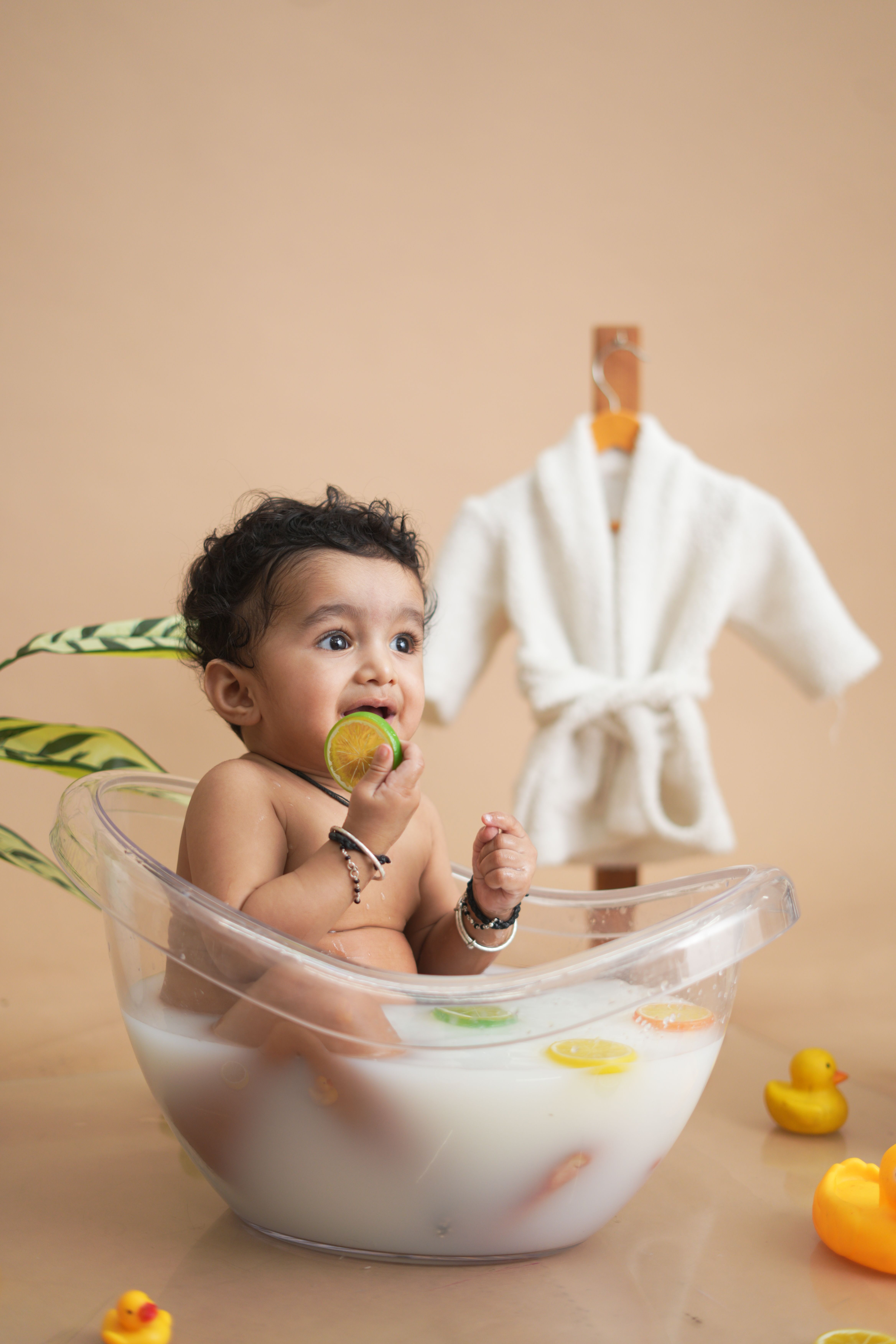 Adorable baby taking a milk bath in a transparent tub, surrounded by rubber ducks and playful toys.