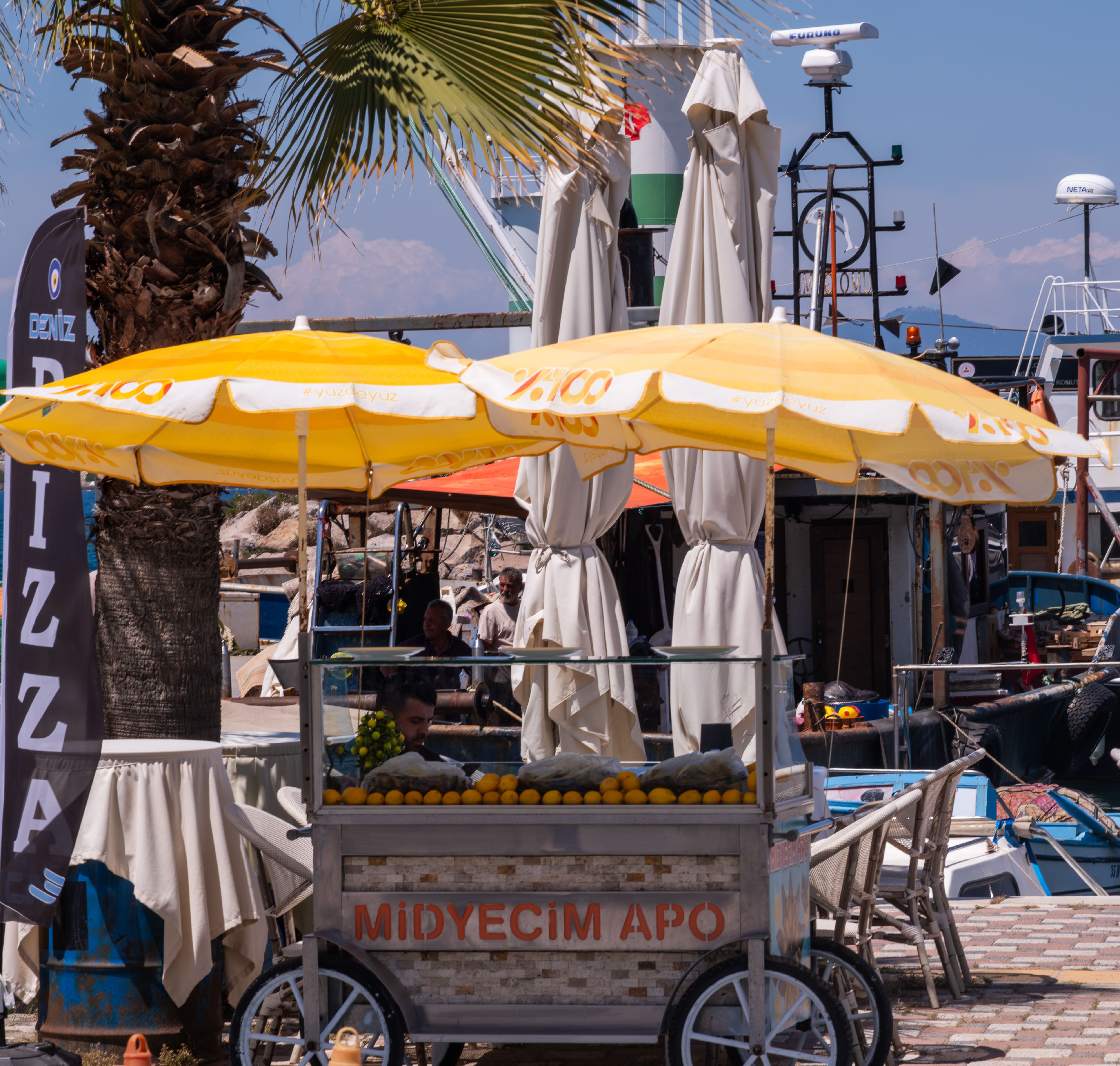 Colorful street food cart under yellow umbrellas in Foça, İzmir, Türkiye, showcasing local charm and vibrant summer atmosphere.