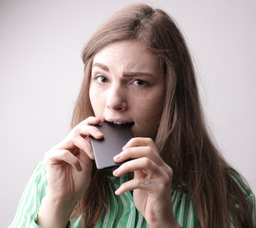 Frowning woman biting smartphone in studio
