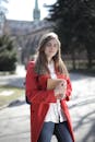 在一个阳光明媚的日子里，一位穿着红色外套的年轻女子在外面拿着一本书微笑