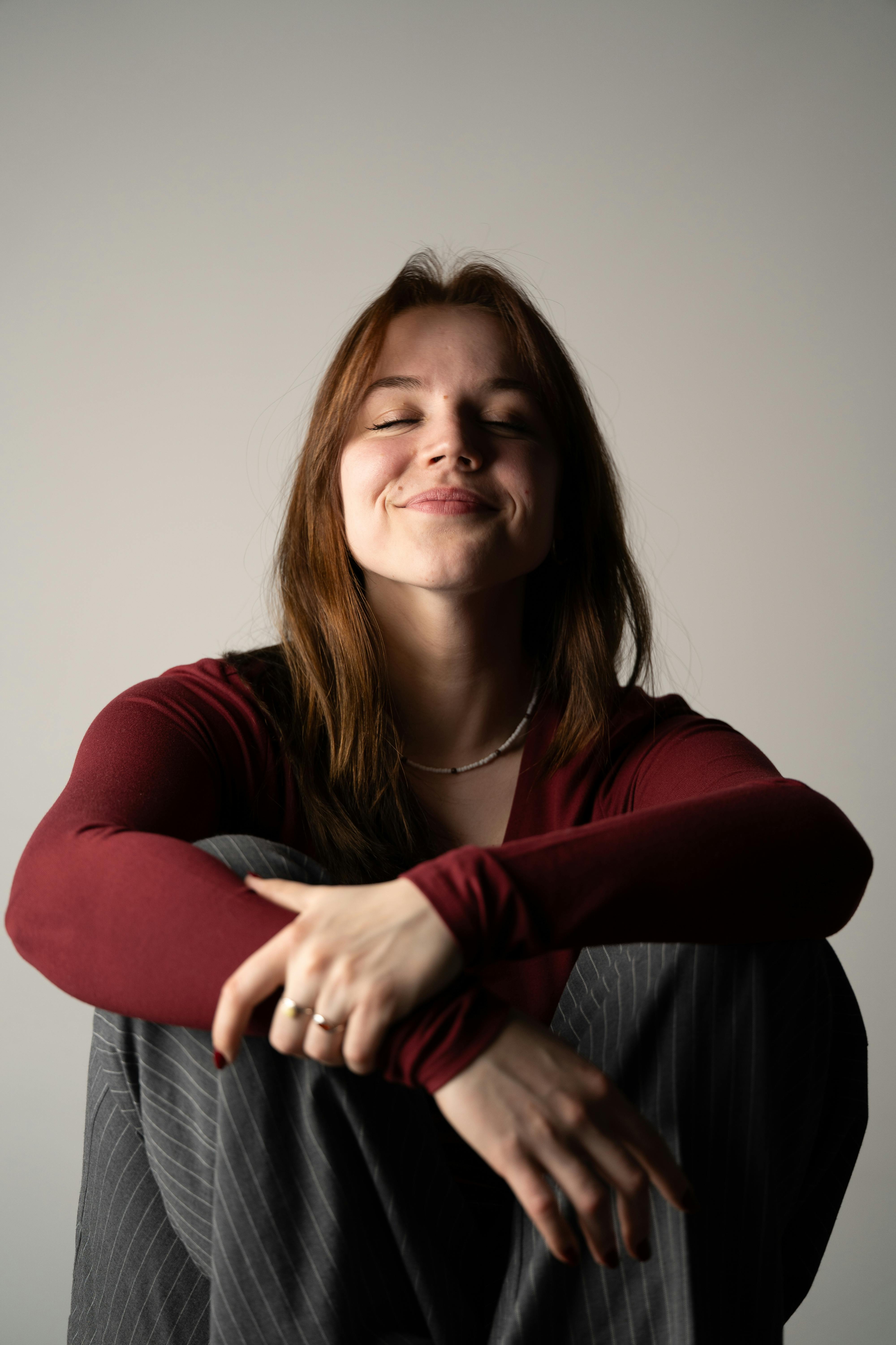 A woman smiling with eyes closed, seated indoors, conveying relaxation and contentment.