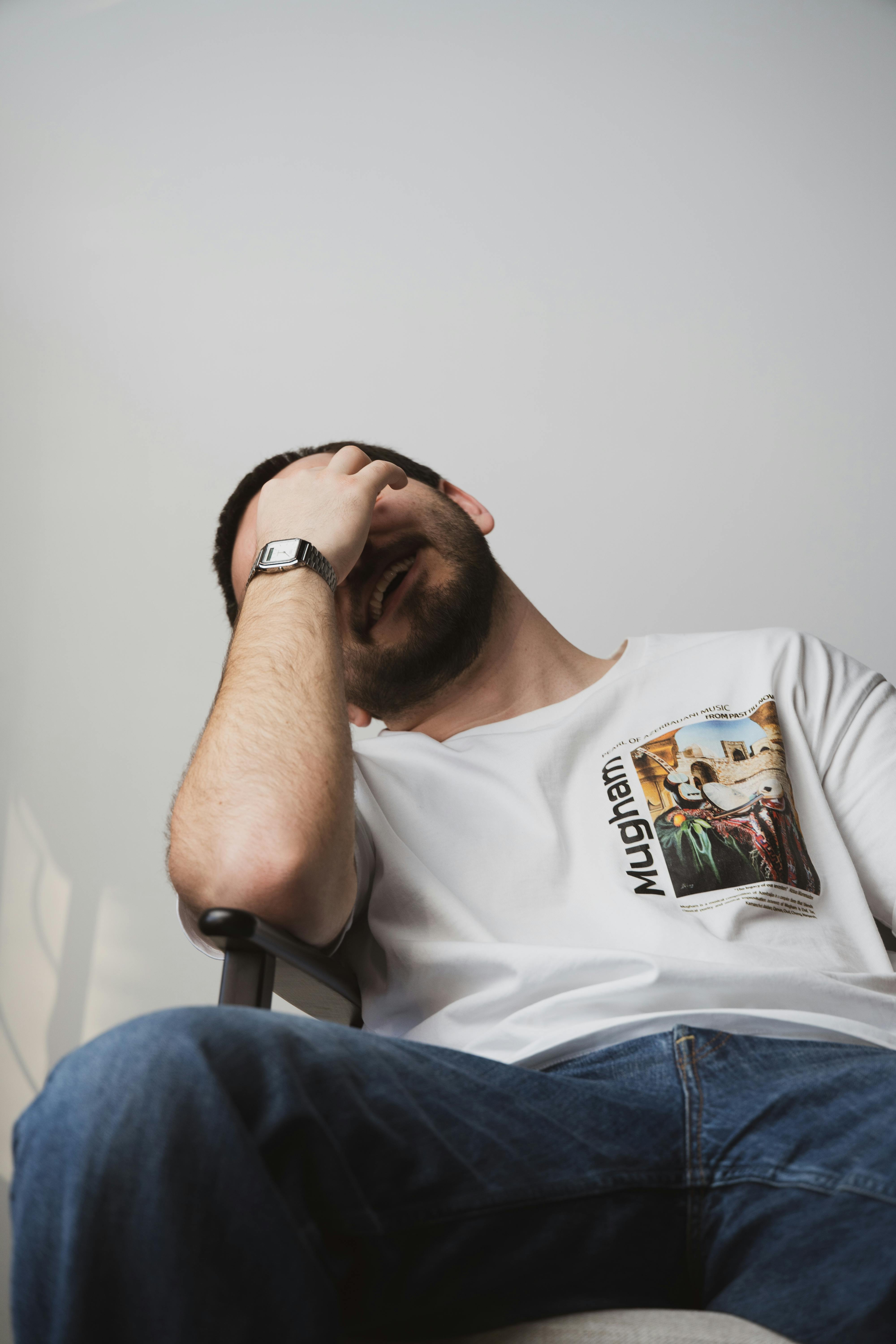 Relaxed man in casual attire covering face while smiling indoors, Riga.