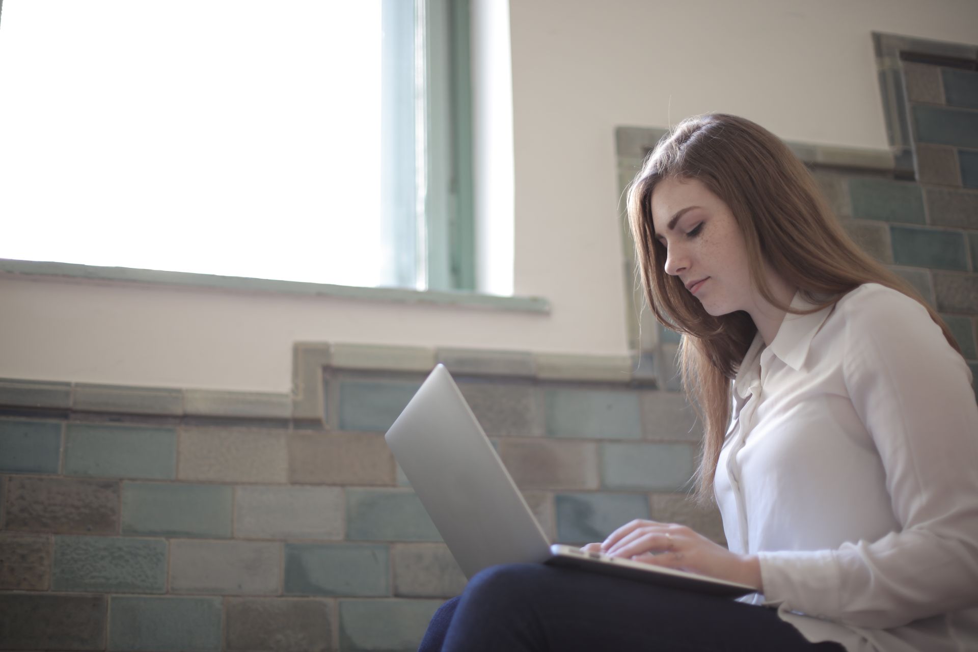 A focused woman in a white shirt using a laptop indoors, ideal for remote work concepts.
