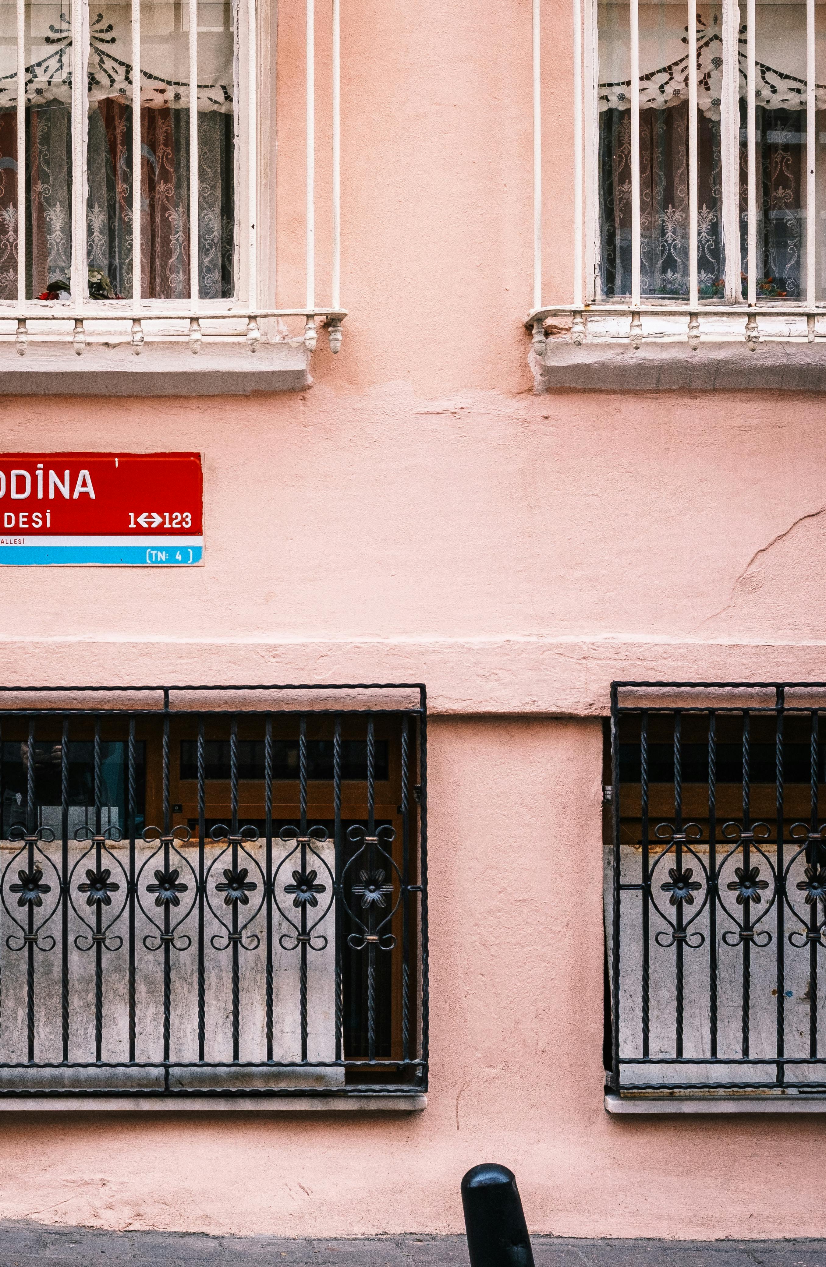 Charming street view of a pastel pink building with decorative window grilles and a street sign.