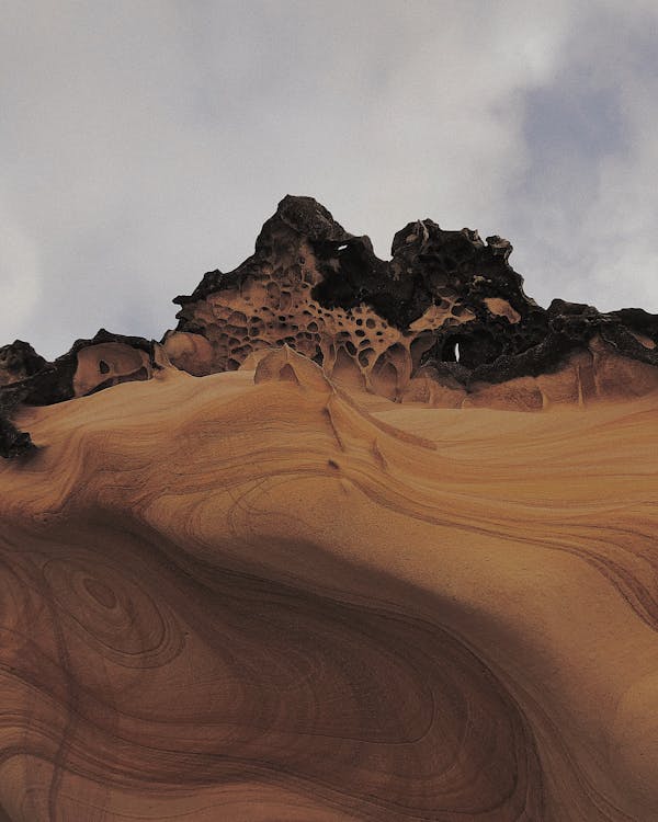 Free Rocky formations on sandy terrain in desert under cloudy sky Stock Photo