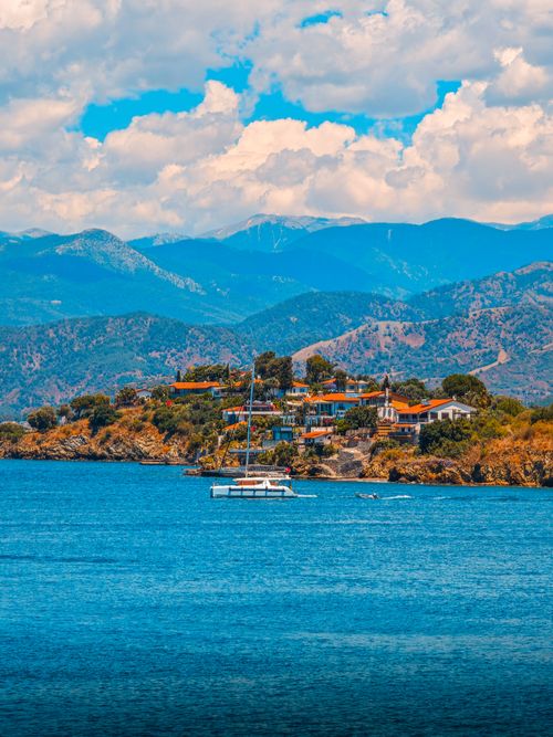 Free Vibrant coastal view of Fethiye, Turkey with mountains and a sailing boat under a sunny sky. Stock Photo