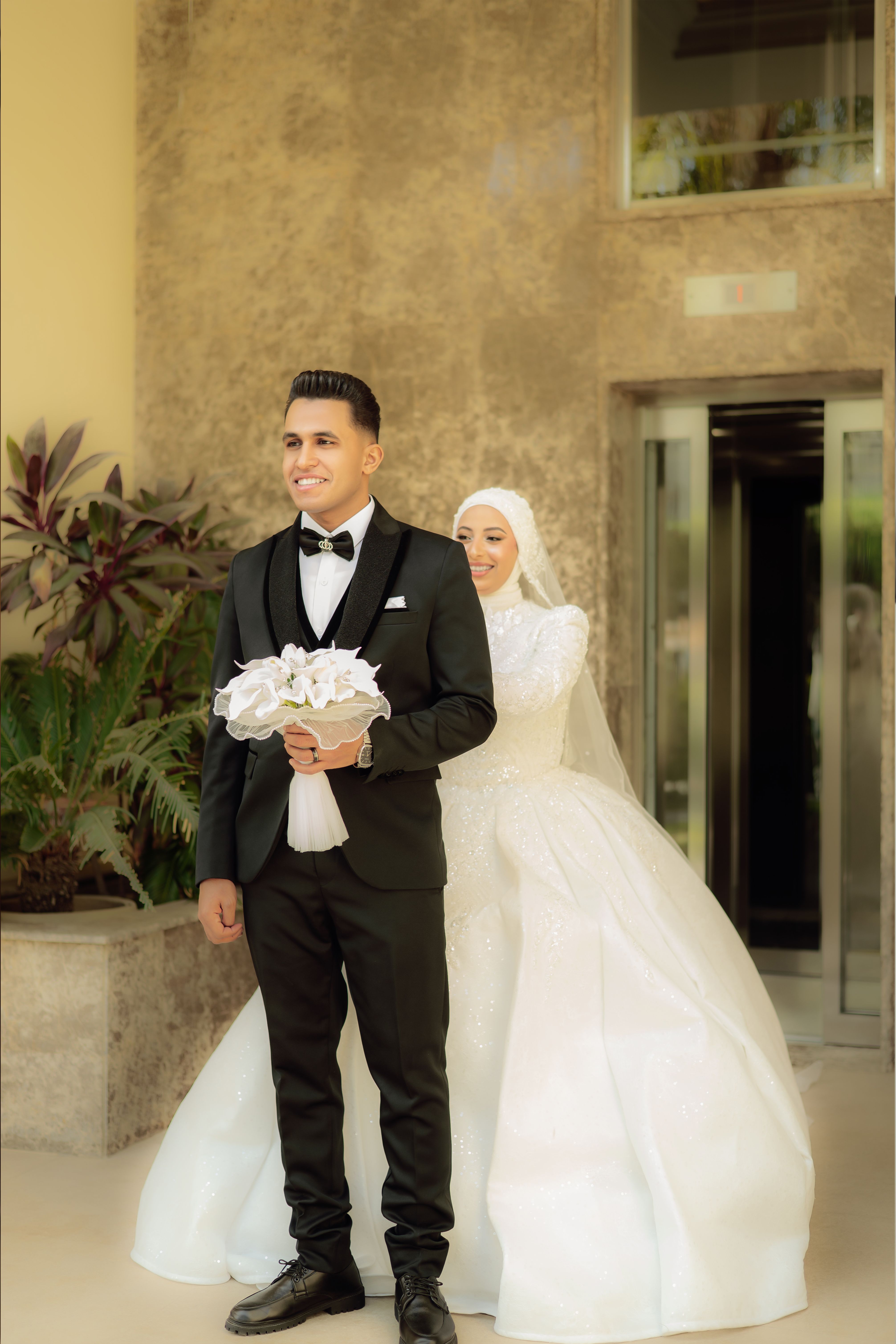 Bride and groom in elegant wedding attire indoors, posing for a formal wedding portrait.