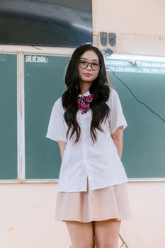 Young woman in school uniform standing before classroom chalkboard.